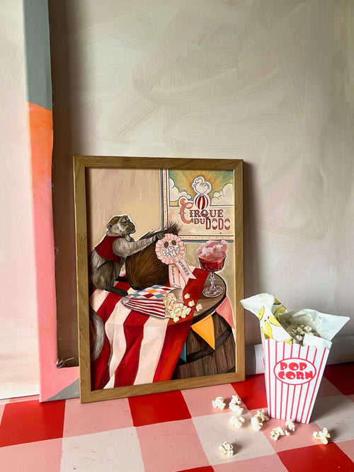 The Coconut Shy Cirque Du Dodo Giclée Art Print by Hôtel Dodo features a vintage-style rat at a circus table with popcorn and a pink drink, set on a checkered floor beside popcorn—evoking the circus vibes of Hôtel Dodo.