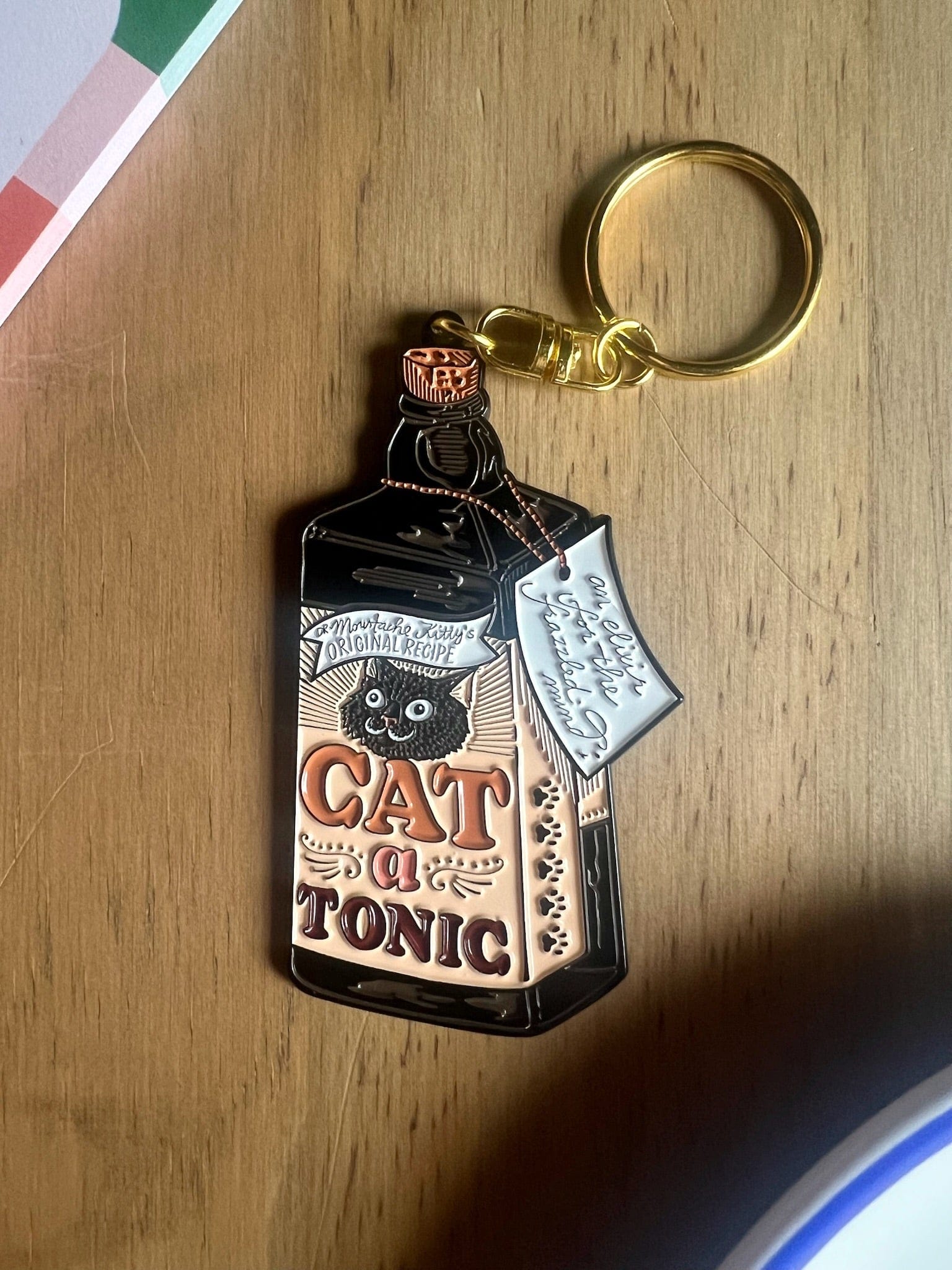 The Hôtel Dodo Catatonic Keyring features a vintage-style "Cat Tonic" bottle design and gold keyring, making this enamel accessory a charming gift for any cat lover.