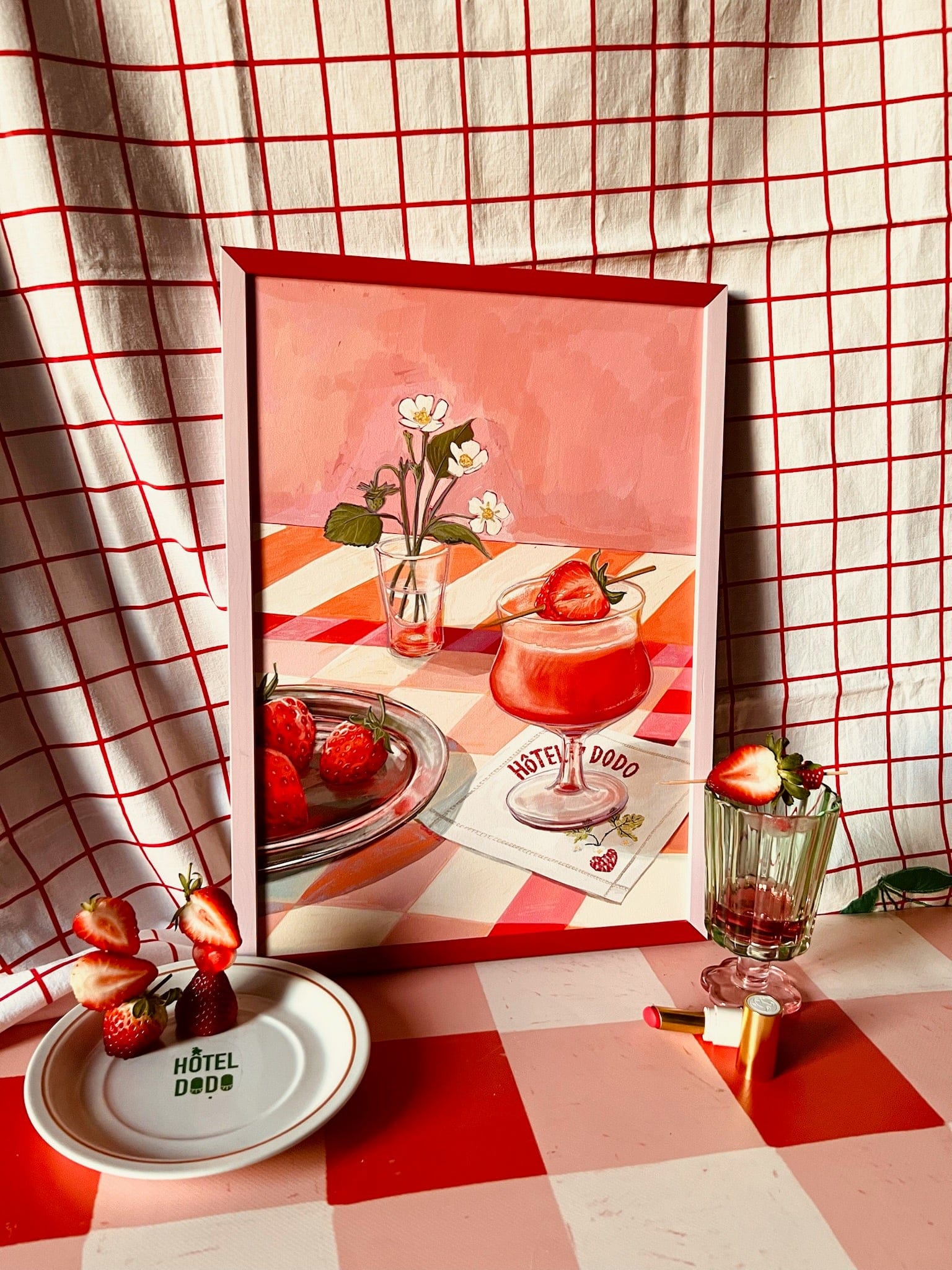 The Daiquiri Dreams Giclée Art Print by Hôtel Dodo depicts strawberries, a dessert, and elegant table settings with checkered fabric in the background, creating a charming scene perfect for kitchen or dining décor.
