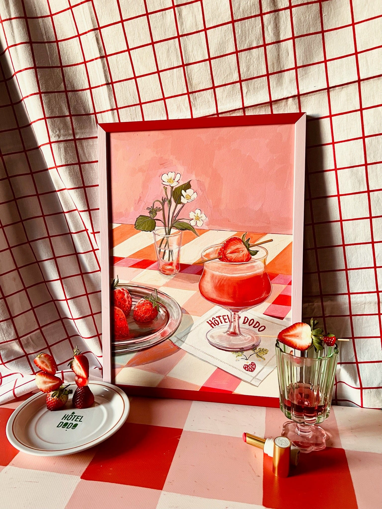The Daiquiri Dreams Giclée Art Print by Hôtel Dodo features strawberries and flowers on a table with a red and white checkered cloth, real strawberries, glassware, plate, lipstick, and echoes of elegant Hôtel Dodo table settings.