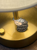 The Doing My Pest Pin by Pins by diedododa features a cartoon rat with a mask and "doing my part" text, displayed on a gold lamp base to symbolize good fortune and prosperity.
