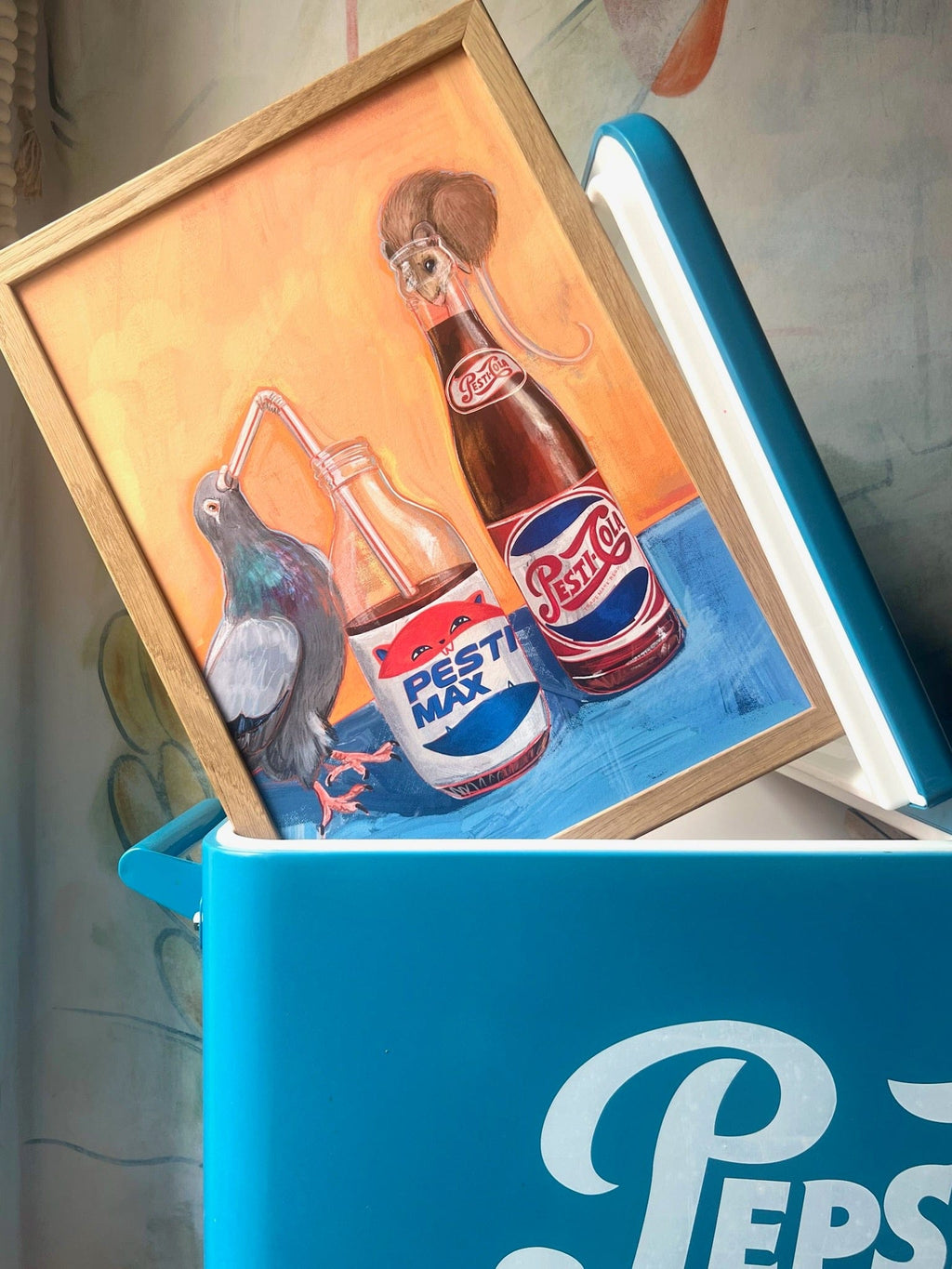 The Pesti Cola Giclée Art Print by Kitsch Kanaveral features a pigeon at a cola can and a mouse on a sugar free bottle, resting atop an open blue Pepsi cooler.