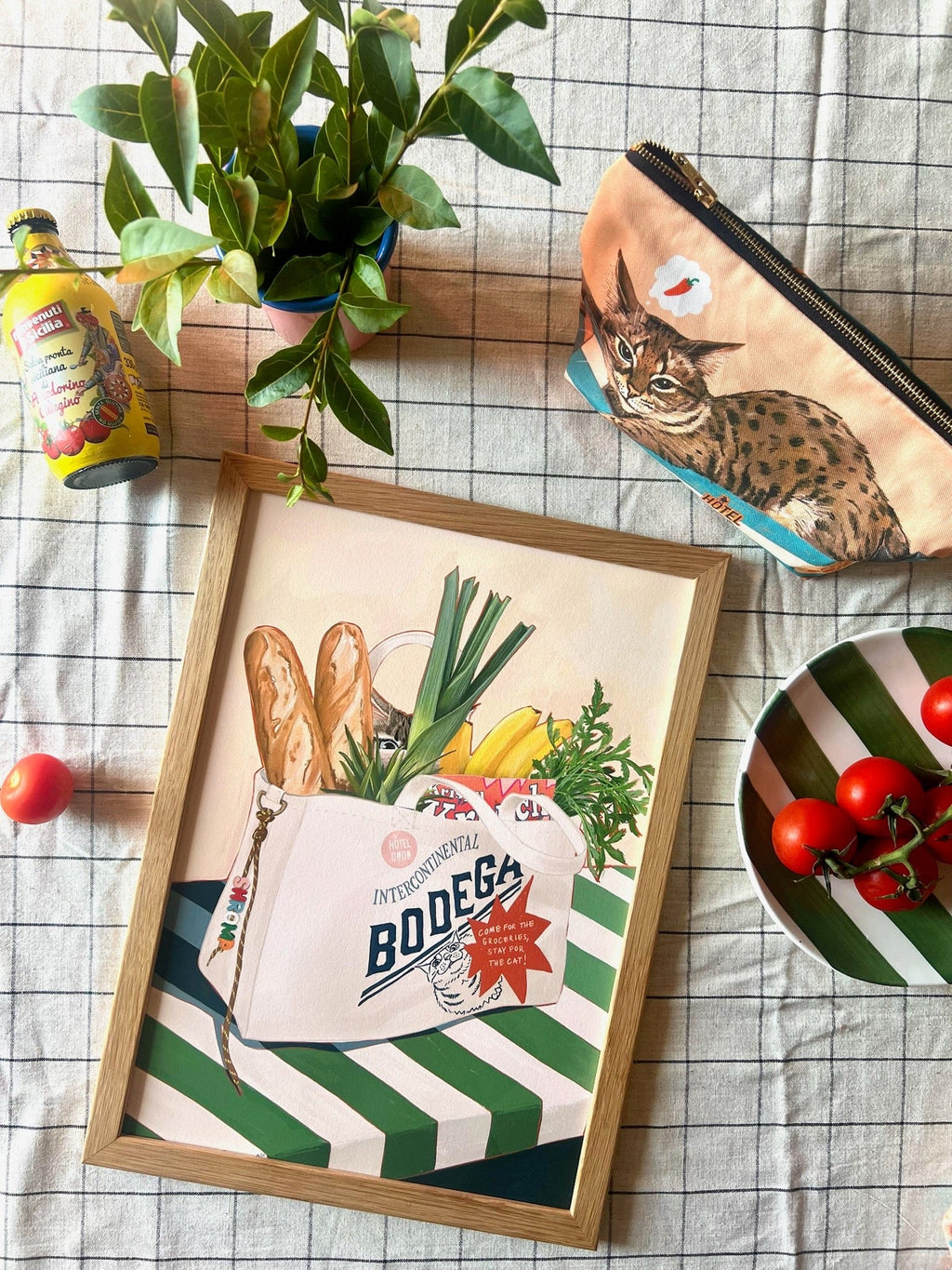 Framed artwork of a bag with groceries and a plant on a checkered tablecloth.
