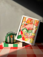 A green striped bag and the Hôtel Dodo Dazed & Sunfused Giclée Art Print are displayed on a red and white checkered surface, with strong sunlight casting bold retro shadows.