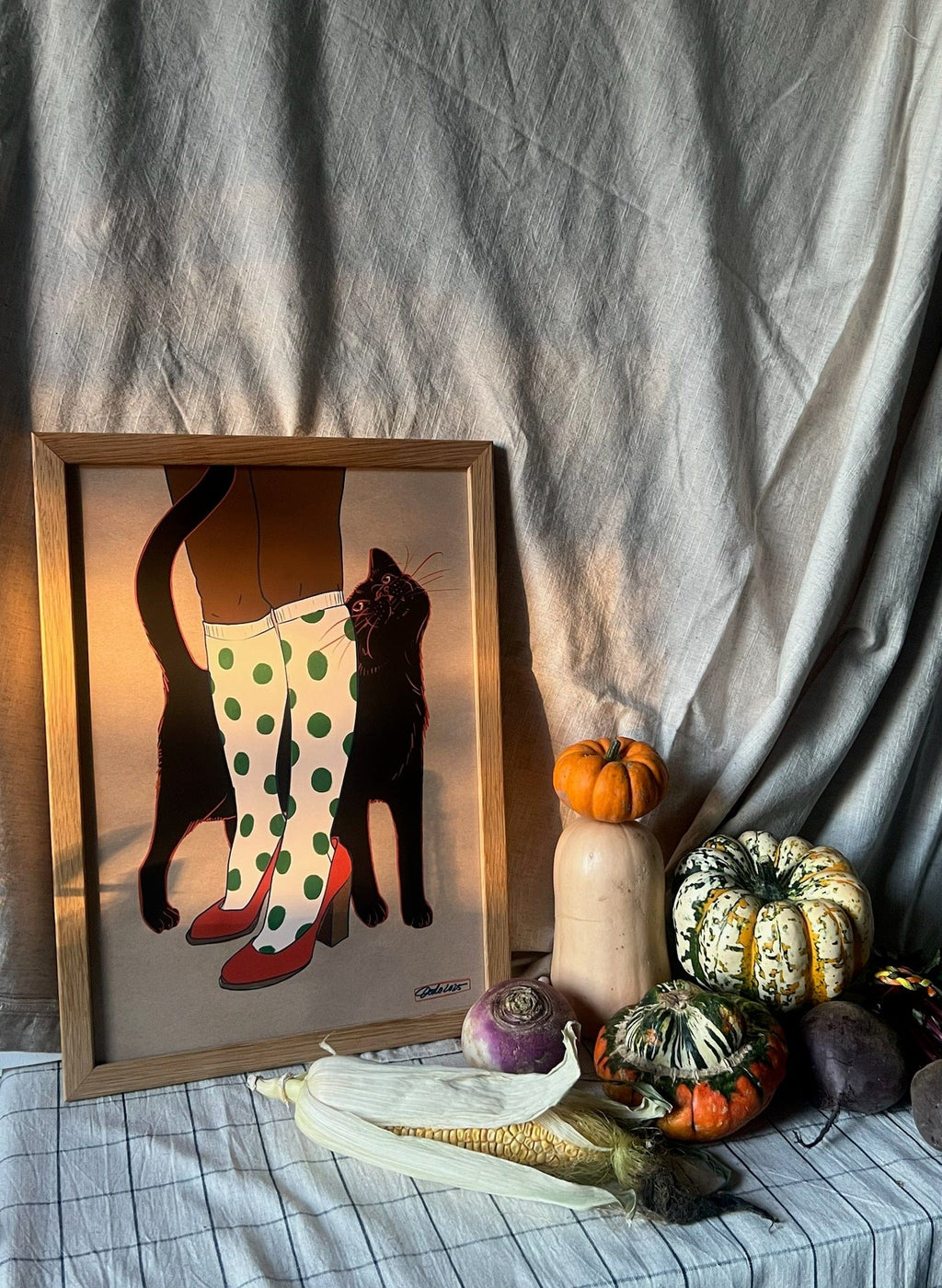 The Encounters of the Purred Kind I Matte Art Print by Beauty and the Beastie features a lucky black cat and polka dot boots, shown framed on a draped table with assorted squash, gourds, and root vegetables.