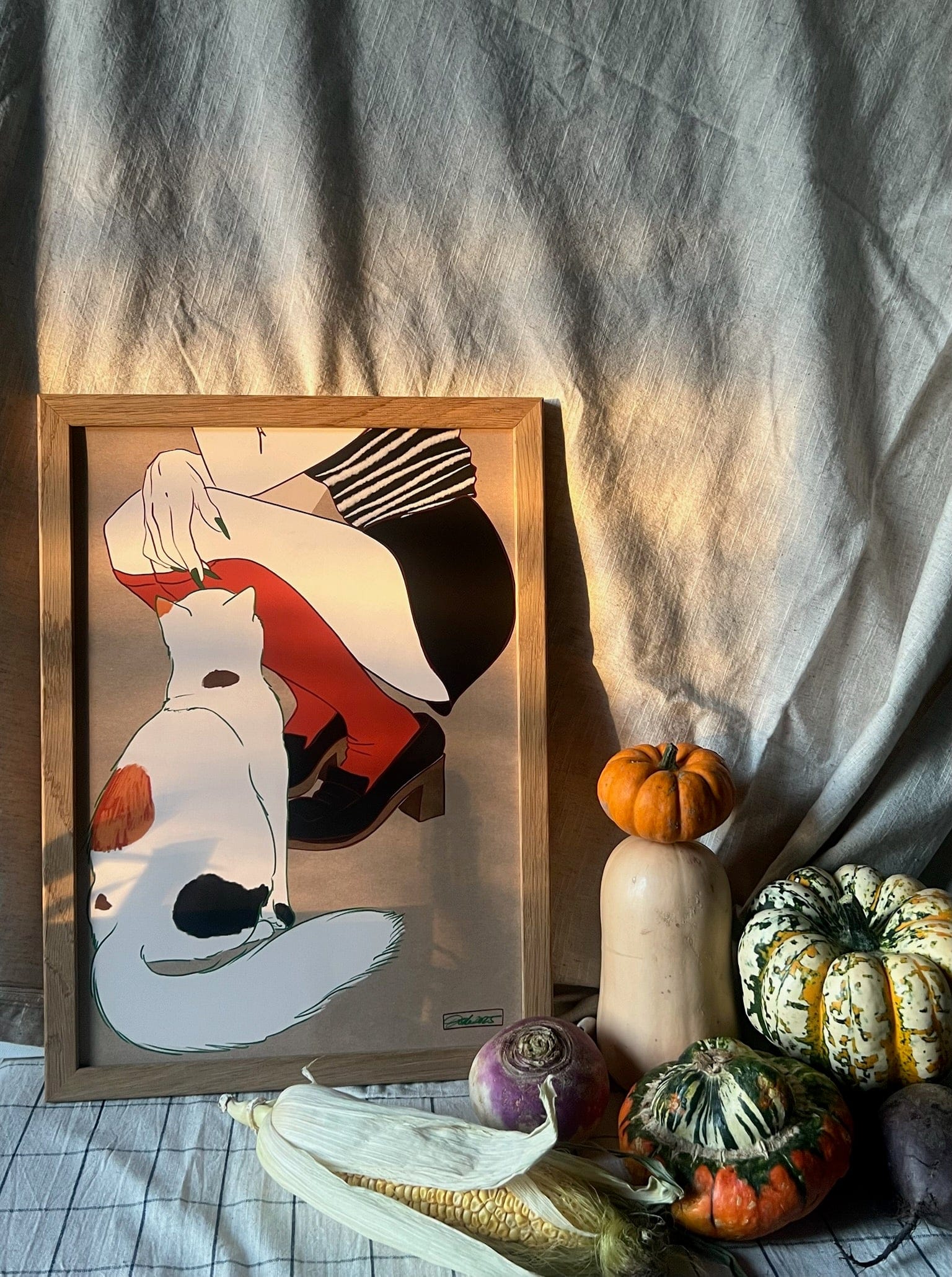 The Encounters of the Purred Kind II Matte Art Print by Beauty and the Beastie features a seated figure with a calico cat, surrounded by squash, a turnip, and corn against a cloth backdrop in natural light, capturing the charm of an animal encounter.