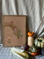 The Spring Snails Matte Art Print by Beauty and the Beastie features a framed hand with snails, set on a table with gourds, corn, and turnip, all against a neutral fabric backdrop.