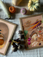 The Earthly Delights Giclée Art Print by Kitsch Kanaveral features framed illustrations of vegetables and animals, displayed on a checkered cloth with squashes, corn, beets, garlic, mushrooms, carrots, and turnip in a harvest festival style.