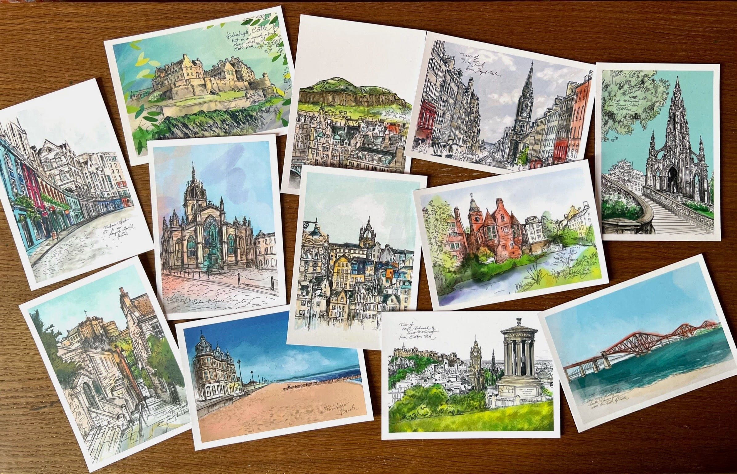 The Enchanting Edinburgh Mini Art Print Set by Essential Edinburgh showcases illustrated prints of iconic city landmarks and scenes, beautifully arranged on a wooden surface.