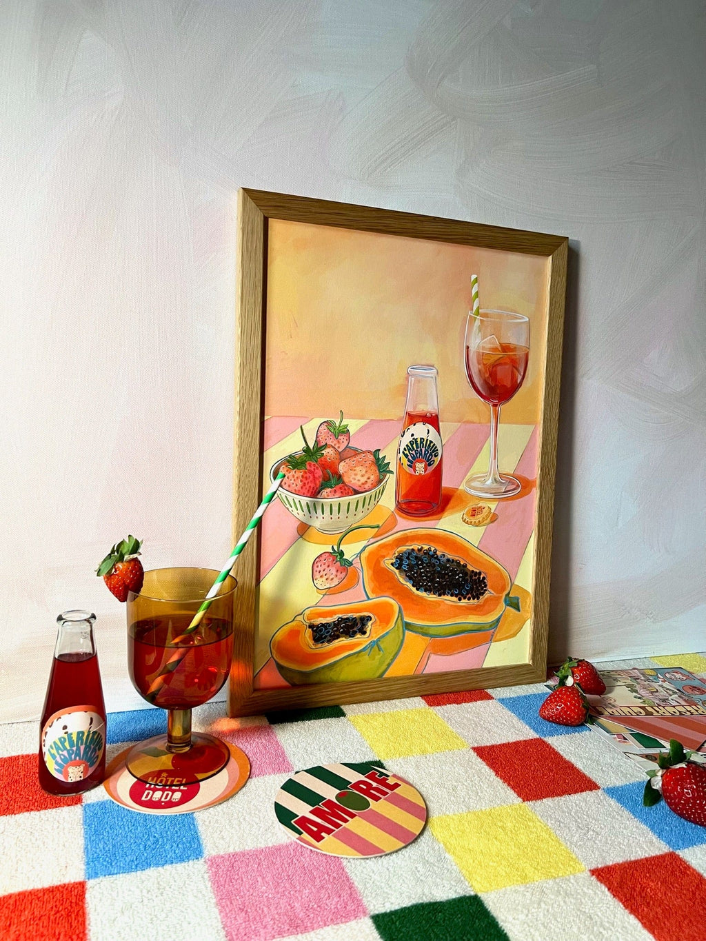The L'Aperitivo Leopardo Giclée Art Print by Hôtel Dodo features a glass and bottle of red vermouth with a straw, strawberries, and playful picnic vibes on a pink-and-yellow checkered background.