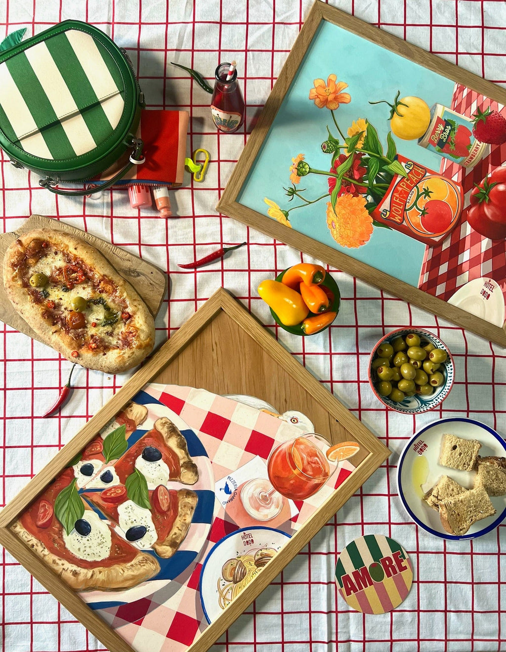 A table at Hôtel Dodo is set with pizza, bread, olives, peppers, a green striped bag, and a drink beneath the vibrant Pizzeria Gabbiano Giclée Art Print—while a curious seagull eyes the tempting meal nearby.