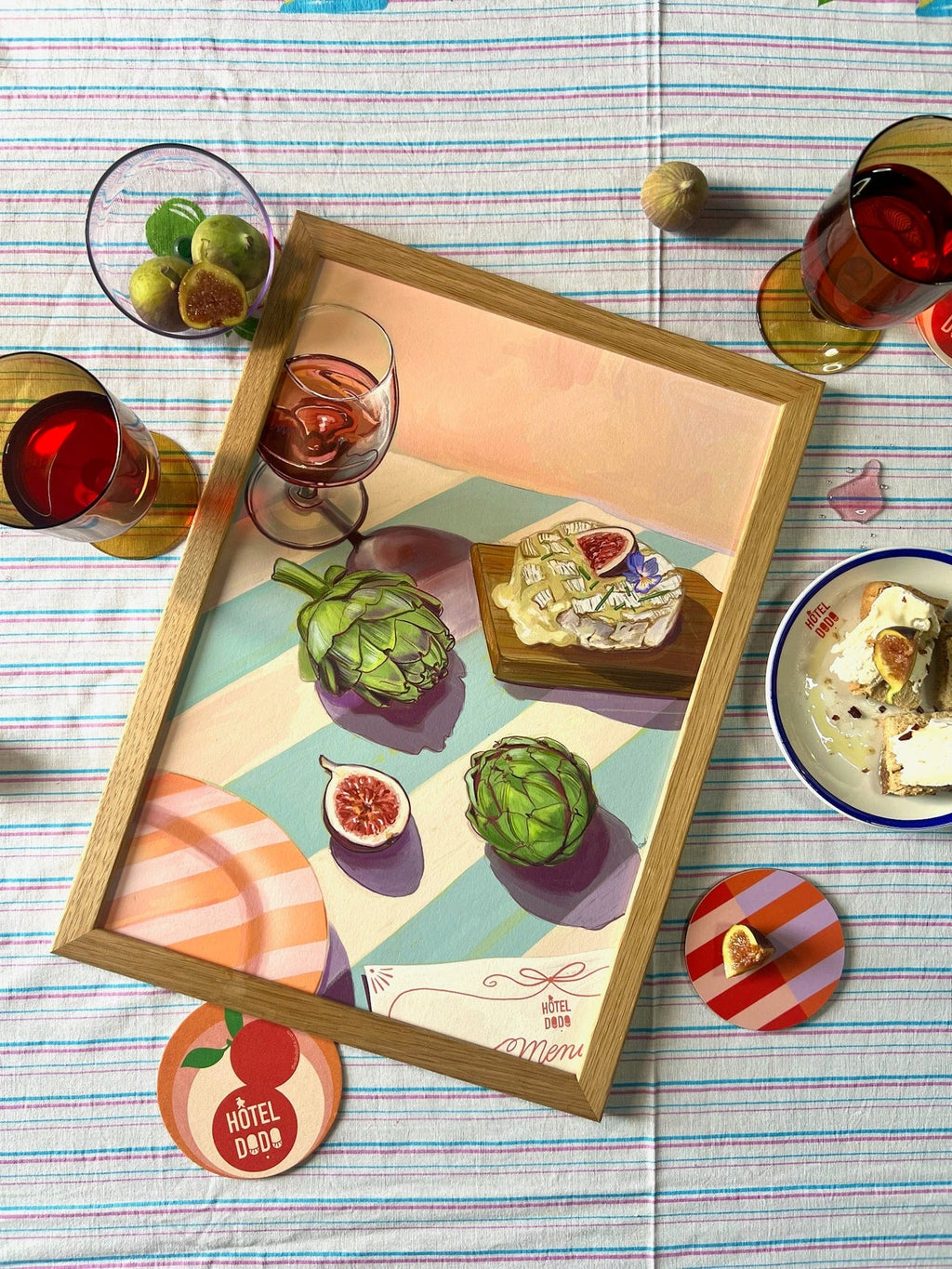 The Figgy Cheese And 'Chokes Giclée Art Print by Hôtel Dodo features artichokes, figs, cheese, and Camembert on a striped tablecloth—an inviting scene inspired by Hôtel Dodo’s signature afternoon menu.