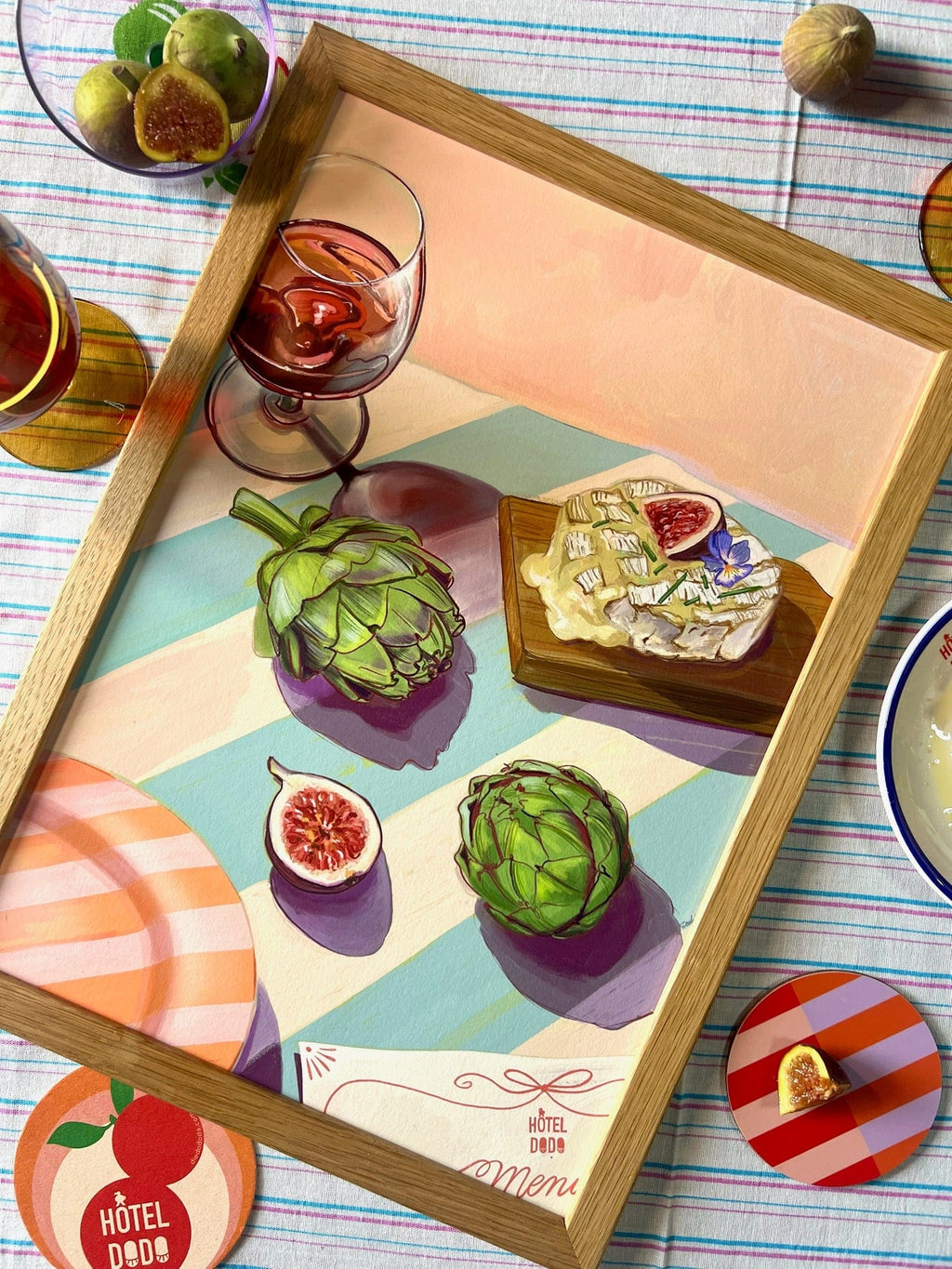 The Figgy Cheese And 'Chokes Giclée Art Print by Hôtel Dodo features a painted still life of artichokes, figs, cheese, and wine—a nod to the brand’s afternoon menu—set on a striped tablecloth.