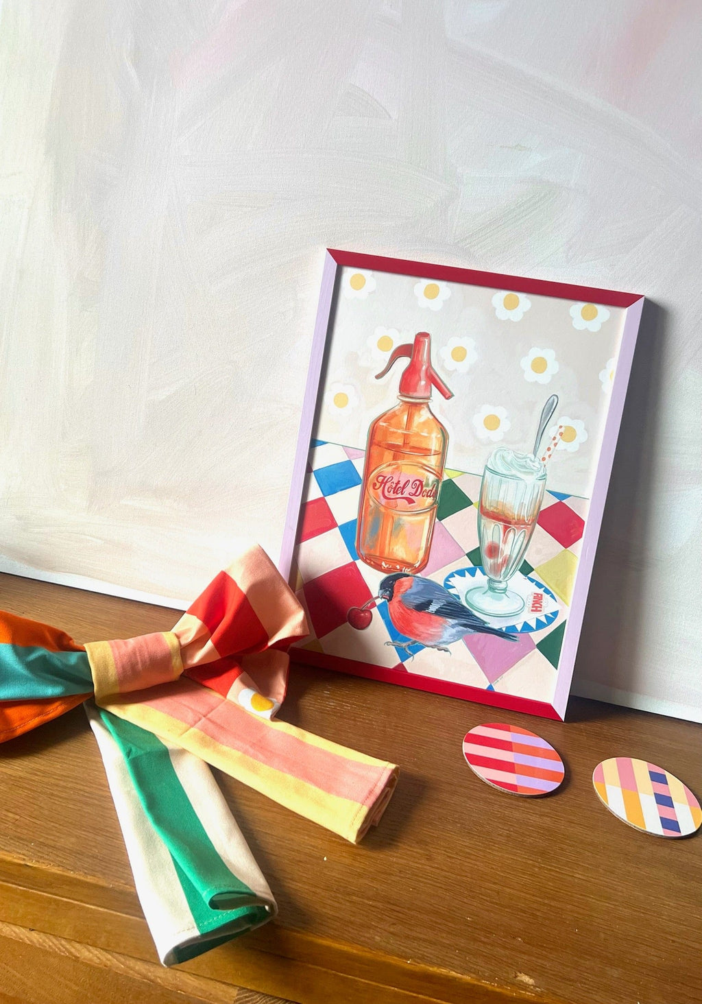 The Fat Finch Soda Giclée Art Print by Hôtel Dodo features a vibrant soda bottle and retro ice cream floats on wood, with striped fabric and two patterned coasters adding charm.