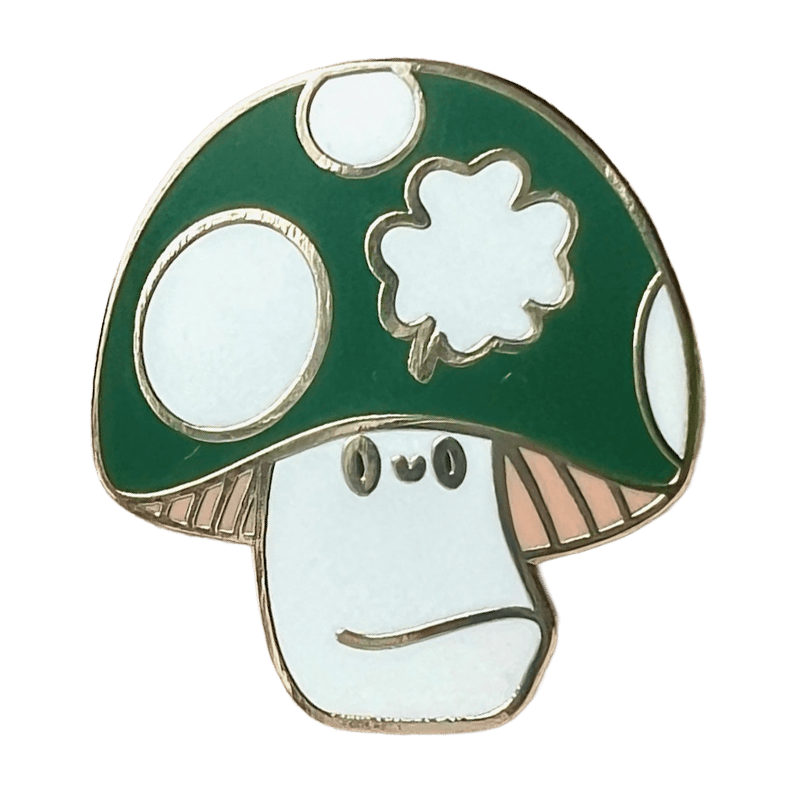The Irish Luckshroom Pin by Pins by diedododa features a cartoon mushroom with a green cap, white spots, and a neutral-faced stem, all outlined in gold.