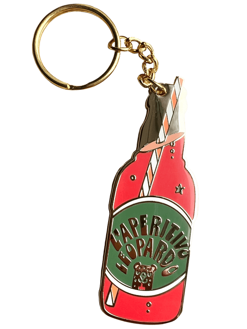 The Hôtel Dodo Aperitivo Keyring features a gold leopard and an enamel charm shaped like a red vintage soda bottle labeled "Aperitivo Leopardo," topped with a striped straw—a playful accessory for your bag.