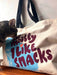 A curious cat sniffs a cotton canvas bag adorned with black handles. The tote, created by Bags by diedododa, reads "But Mostly I Like Cats" in bold, colorful letters.