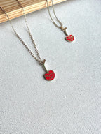 Two Mon Chérie necklaces with captivating red mushroom pendants lie gracefully on a light gray fabric, a wooden plank subtly visible in the background.