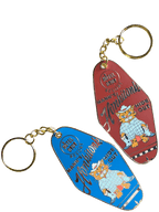 Two vintage-style Hôtel Dodo keychains, Hank's Honkitonk Hideout: one blue, one red. Each has a cartoon cat in a hat with "Kankakee" and "Mammoth Hide Out" text. These are attached to gold-colored rings, adding charm to any collection.
