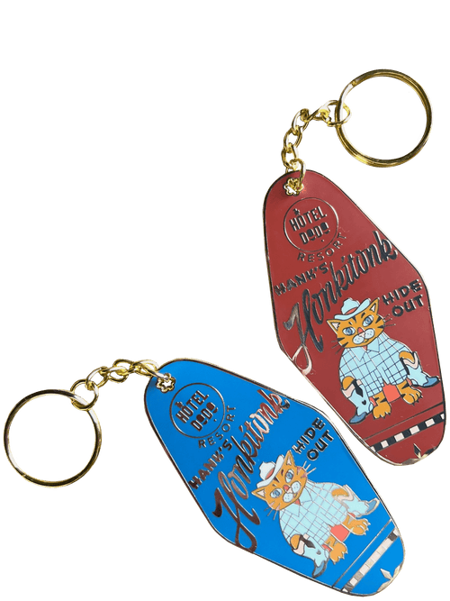 Two vintage-style Hôtel Dodo keychains, Hank's Honkitonk Hideout: one blue, one red. Each has a cartoon cat in a hat with "Kankakee" and "Mammoth Hide Out" text. These are attached to gold-colored rings, adding charm to any collection.