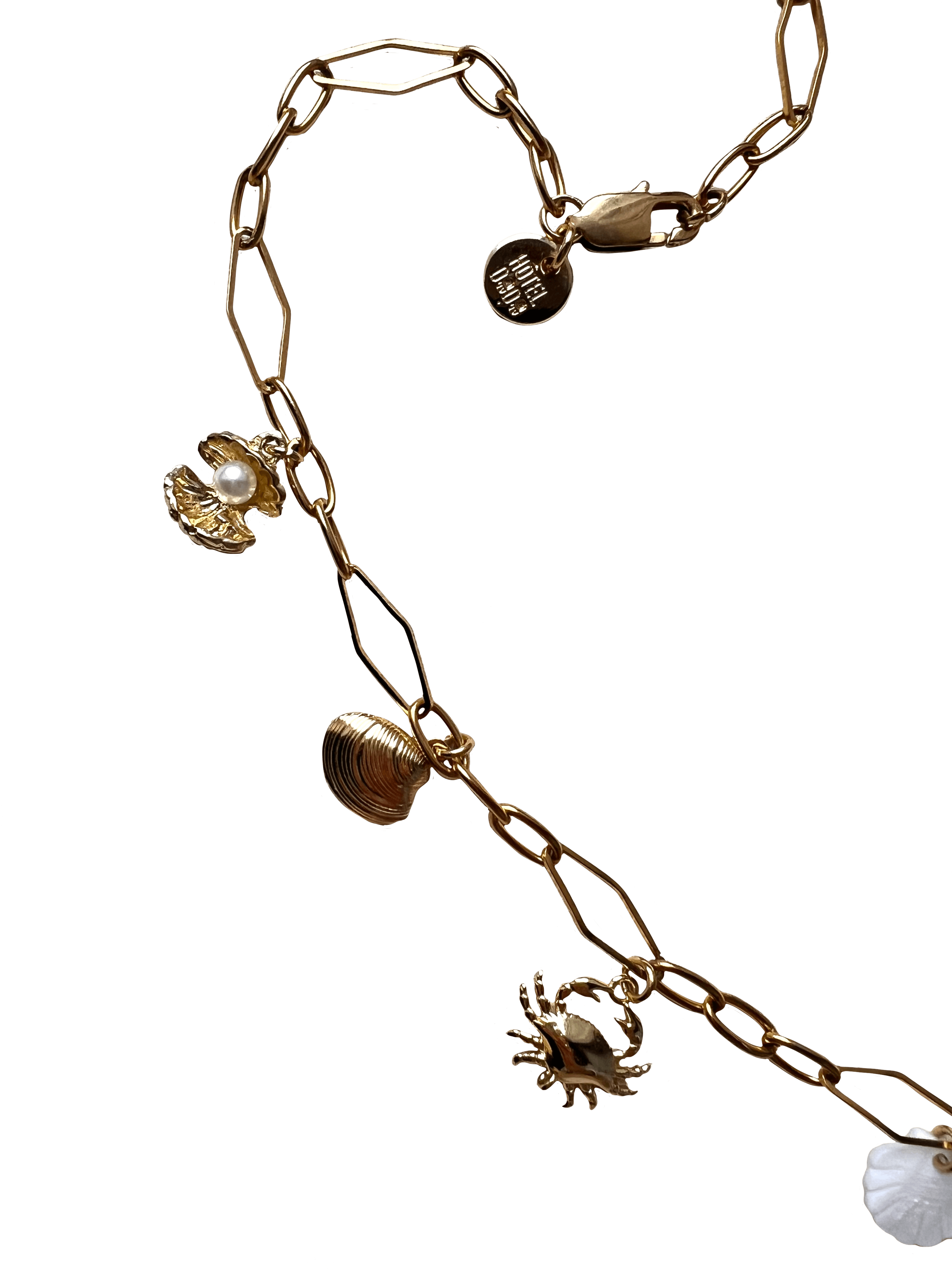 The Seaside Treasures Necklace by Necklaces, featuring gold-plated seashell charms including a crab, a shell, and a circular pendant with text, set against a black background.