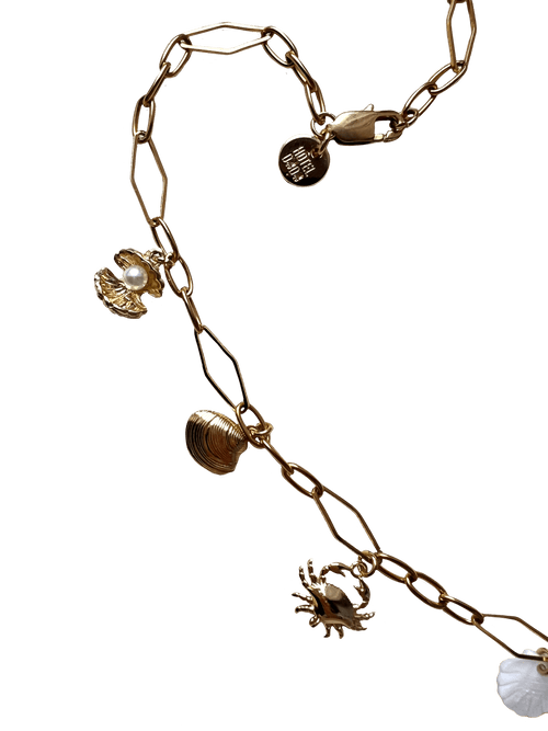 The Seaside Treasures Necklace by Necklaces, featuring gold-plated seashell charms including a crab, a shell, and a circular pendant with text, set against a black background.