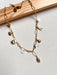 The Seaside Treasures Necklace from Necklaces features a gold chain adorned with charming seashells, a starfish, and delicate leaves, beautifully displayed against a light fabric background framed in wood. This exquisite 18K gold-plated piece is ideal for seafood enthusiasts wanting to infuse their jewelry collection with a coastal vibe.