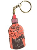 The Hôtel Dodo Bodega Cat Hot Sauce Keyring is a keychain and bag charm shaped like a hot sauce bottle, featuring a cartoon bodega cat with “Bodega Cat Hot Sauce” and “Senior Spicy” on an enamel tag.