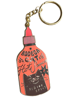 The Hôtel Dodo Bodega Cat Hot Sauce Keyring is a keychain and bag charm shaped like a hot sauce bottle, featuring a cartoon bodega cat with “Bodega Cat Hot Sauce” and “Senior Spicy” on an enamel tag.