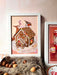 The Gingerpest House Giclée Art Print by Kitsch Kanaveral features a gingerbread house artfully illustrated with a deer and a bird, surrounded by nuts and presented on a fluffy surface.