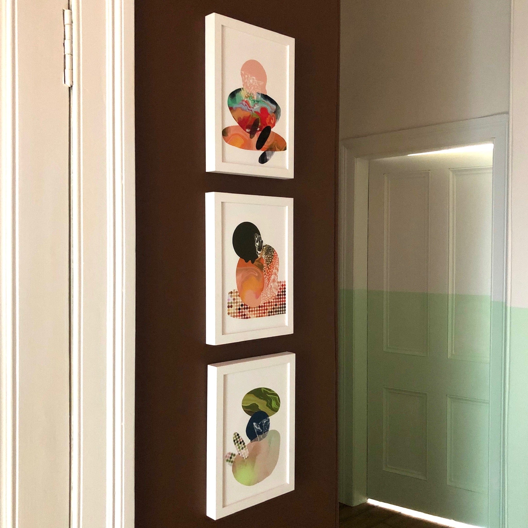 Three Catastract Tangerine Tiger Matte Art Prints hang vertically on a brown hallway wall, beside a partially open door and a green-accented wall, adding subtle beachy holiday vibes.