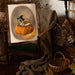 A Grumpy Spiced Pumpkin Giclée Art Print from Kitsch Kanaveral, featuring a toad in a witchy hat sitting on a pumpkin, rests on a chair surrounded by rustic decor and dried plants, setting the perfect autumn scene.