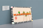 The Shromps Magnifique Matte Canvas Print features bold “MAGNIFIQUE” lettering, a parrot, palm trees, and tropical accents, creating a resort-inspired look beside a Hôtel DOBO business card on a gray wall.