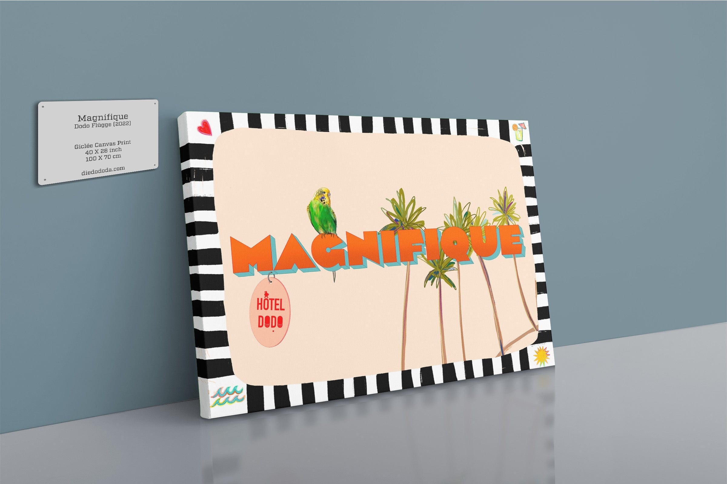 The Shromps Magnifique Matte Canvas Print features bold “MAGNIFIQUE” lettering, a parrot, palm trees, and tropical accents, creating a resort-inspired look beside a Hôtel DOBO business card on a gray wall.