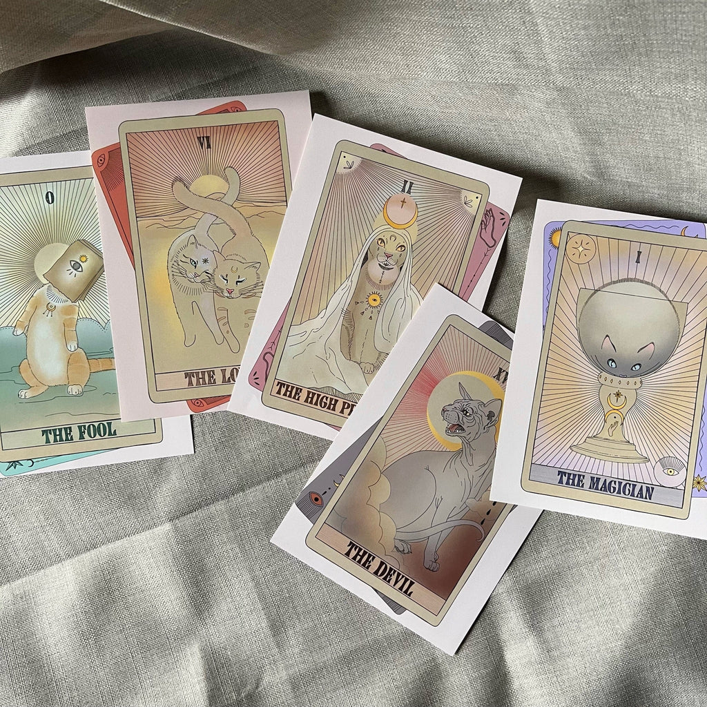 The Lovers Matte Art Print by Tarot Cats features vintage-inspired illustrations of classic tarot cards, including The Fool, The Lovers, The High Priestess, The Devil, and The Magician on a light fabric surface.